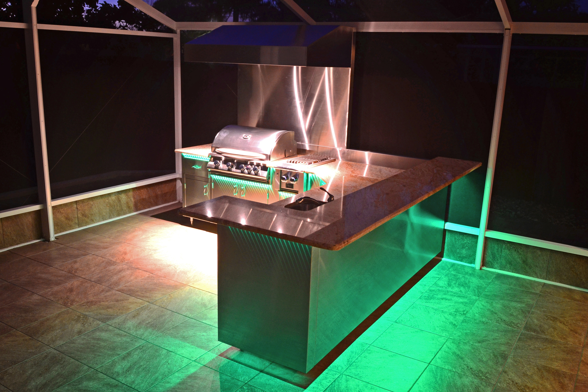 An outdoor kitchen with green lighting in an enclosed patio, to illustrate how outdoor kitchen lighting enhances the look of outdoor spaces